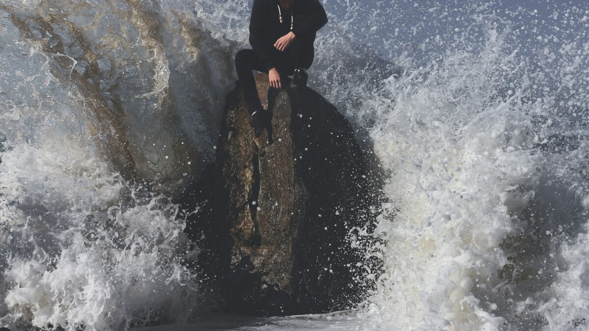 man seating on stone in between waving sea